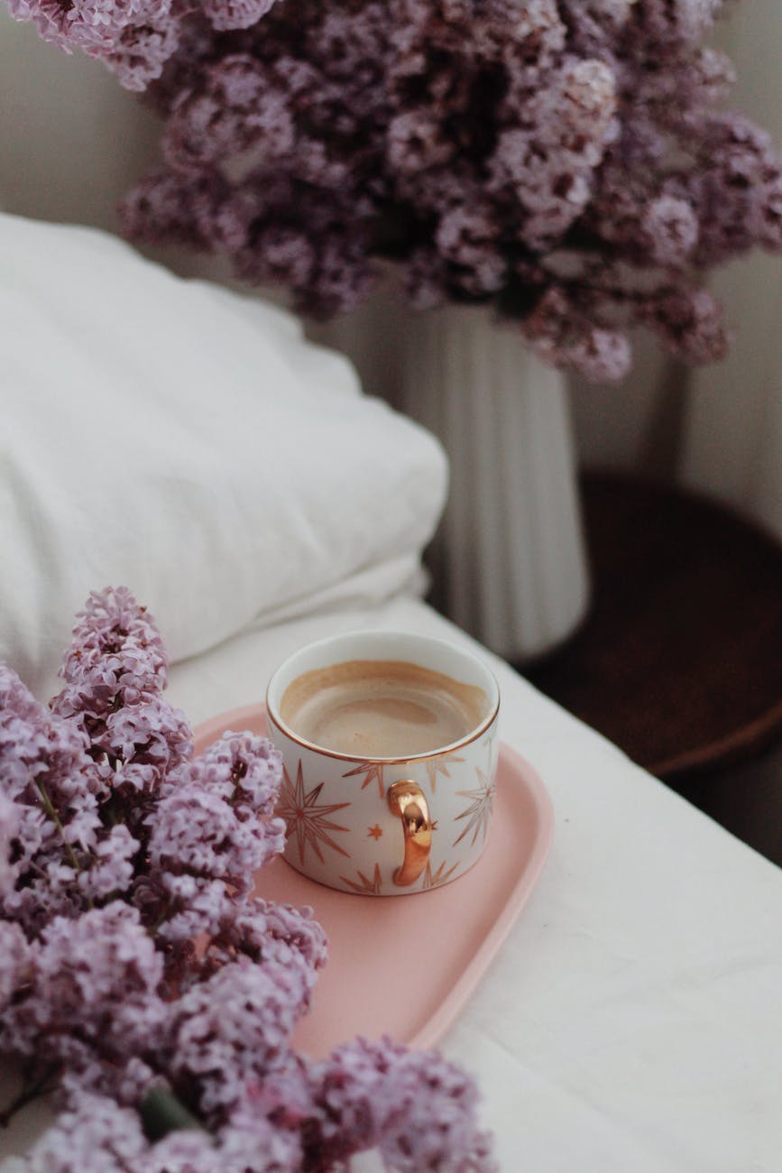 cup of coffee on tray on bed decorated with lilac